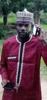 Man in red traditional attire holding a phone outdoors.