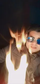 Man with sunglasses surrounded by fire in dark background.