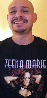 Man smiling in a Teena Marie T-shirt with a warm background.