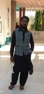 Man in traditional attire standing indoors with soft lighting.