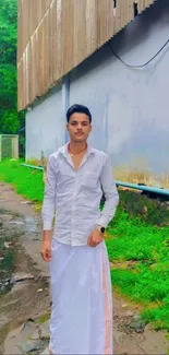 Man in white traditional attire standing on a green nature path.