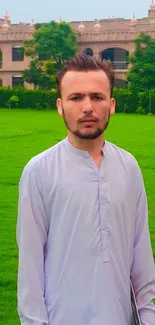 Person in traditional outfit standing in a lush garden with historic architecture.