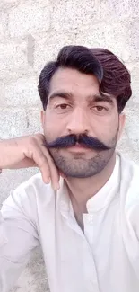 Man with mustache in white shirt, brick wall background.