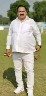 Man in white attire standing outdoors on a sunny day.