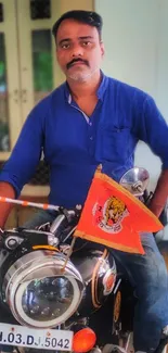 A man in a blue shirt on a motorcycle with an orange flag.