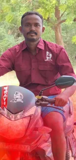 Man on motorcycle in lush green setting with red hues.