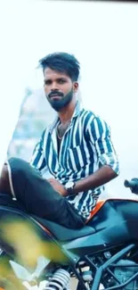 Man in striped shirt sitting on a motorcycle.