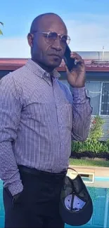 Man in a plaid shirt on phone near a pool.