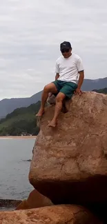 Man sitting on a rocky cliff overlooking the ocean and cloudy sky.