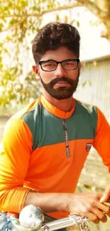 Man in orange shirt by tree, relaxed pose.