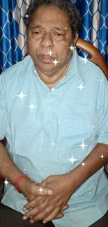 Man sitting on chair with blue curtains in background.