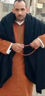 Man with orange cloak and beads in urban setting.