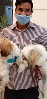 Man wearing a mask holding two dogs indoors.