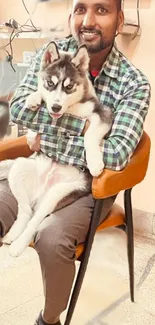 Man sitting with husky puppy on chair in cozy setting.