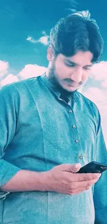 Man with smartphone against a blue sky and clouds, emanating tranquility.