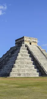 Mayan pyramid with blue skies and grassy field in the foreground.