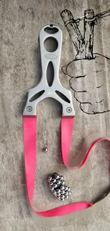 Metallic slingshot with pink bands on textured gray background.