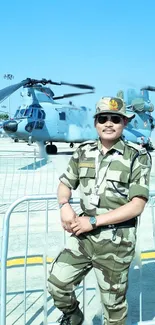 Soldier in camo with helicopter in background on clear day.