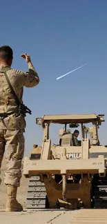 Soldier directing vehicles in desert terrain.