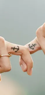 Two fingers with anchor tattoos touching gently.