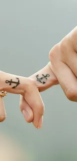 Two fingers with anchor tattoos on a beige background.