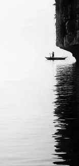 Silhouette of fisherman on boat by a cliff in a minimalist black and white scene.