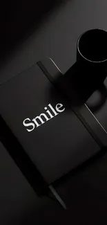 Black notebook with 'Smile' next to a black coffee cup on a dark background.