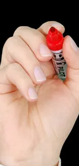 Hand holding a red marker on a black background wallpaper.