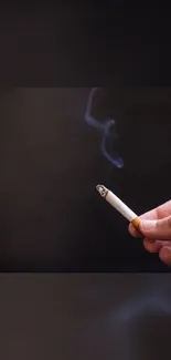 Hand holding a cigarette with smoke on a dark background.