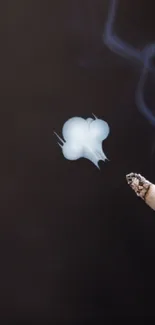 Hand holding a smoking cigarette on a dark background with artistic smoke.