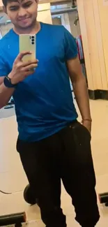 Gym mirror selfie with blue shirt and phone in hand.