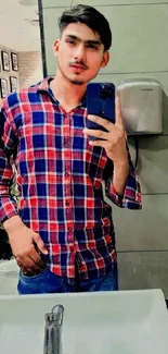 Person taking a mirror selfie in a red and blue plaid shirt.