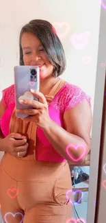 Mirror selfie with pink neon heart effects on phone wallpaper.