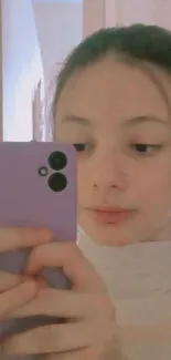 Young person takes a mirror selfie with a purple phone.