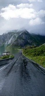 Misty road leading to mountains with lush greenery and cloudy sky.