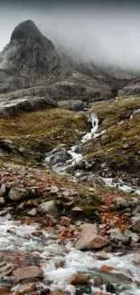 Misty mountain with cascading stream in rocky terrain.