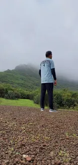 A lone explorer stands on a misty mountain surrounded by lush greenery.