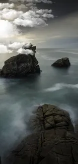 Misty ocean waves surround rugged rocks under a moody gray sky.