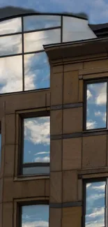 Modern building with reflective glass panels showing sky and clouds.