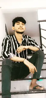 Young man in striped shirt sits stylishly on stairs.