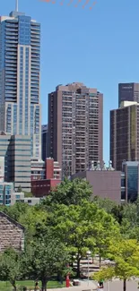 Vibrant city skyline with clear blue sky and lush green trees in the foreground.