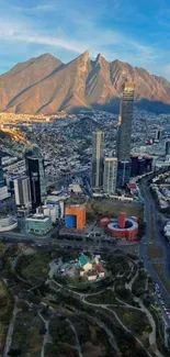 Aerial cityscape with mountains and skyscrapers under a clear blue sky.