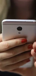 Close-up of a hand holding a modern mobile phone with red nails.