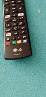 Black remote control on a teal surface.