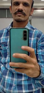 Man takes selfie with turquoise phone in barbershop mirror.