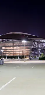 Modern stadium exterior with night lights glowing and empty parking lot.