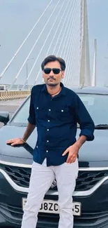 Man stands next to a sleek black car on an urban bridge.