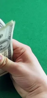 Hands counting dollar bills on a vibrant green surface.