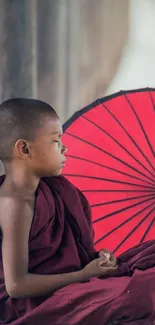 Young monk by red umbrella in contemplation.