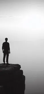 Silhouette of a person on a cliff in monochrome, embracing solitude.